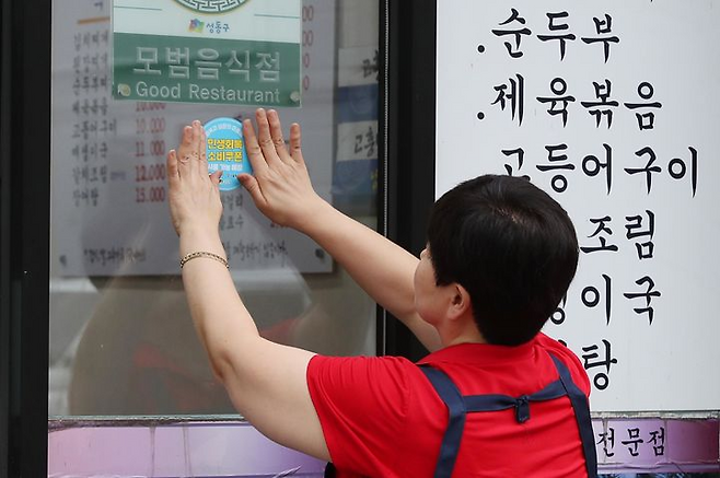 A restaurant worker in Seoul affixes a special sticker signaling businesses that accept stimulus coupons. The stimulus program, which starts Monday, aims to alleviate the cost-of-living burden and stimulate the sluggish economy. (Newsis)