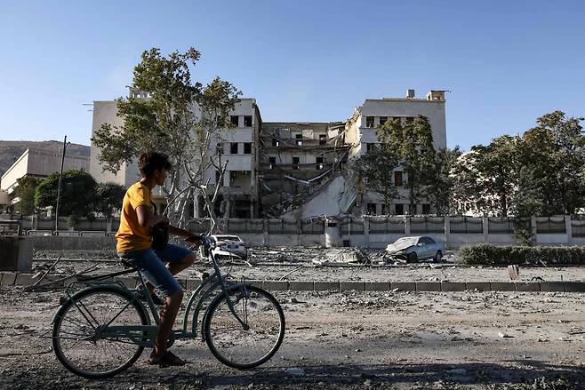 시리아 수도 다마스커스에 거주하는 한 청년이 이스라엘 공습으로 부서진 시리아 국방부 청사를 지나고 있다. [AFP]