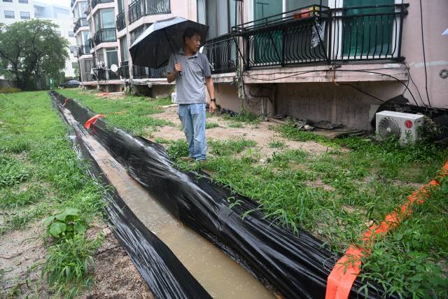 ▲ 춘천 지역의 한 노후 아파트 내에 다수의 싱크홀이 생겨 주민들이 불안해 하고 있는 가운데 폭우가 내린 지난 18일 아파트 관계자가 싱크홀 옆에 임시로 만든 배수로를 살펴보고 있다.  방도겸 기자