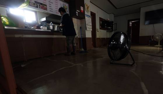 지난 21일 경남 산청군 신안면의 한 식당에서 식당 관계자가 컵라면을 먹기 위해 도구를 챙기고 있다. 식당 관계자는 "호우 여파로 단전, 단수, 가스 공급이 중단됐고, 선풍기 돌릴 전기를 위층에서 끌어다가 쓰는 중이다"고 설명했다. 연합뉴스