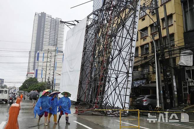 [케손=AP/뉴시스] 19일(현지 시간) 필리핀 케손시에서 제6호 태풍 위파 영향으로 구조물이 휘어진 가운데 시민들이 인근을 지나가고 있다. 2025.07.22.