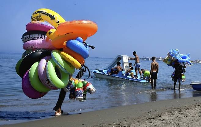 7월 18일 금요일 알제리 알제 해변에서 부표를 판매하는 상인들이 걸어가고 있다. AP 연합뉴스