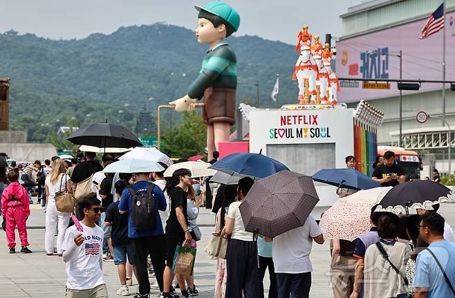 무더위가 이어진 4일 서울 종로구 광화문광장에 마련된 넷플릭스 오징어 게임 체험존에 관광객들이 양산을 쓰고 대기하고 있다. 2025.7.4/뉴스1 ⓒ News1 김도우 기자