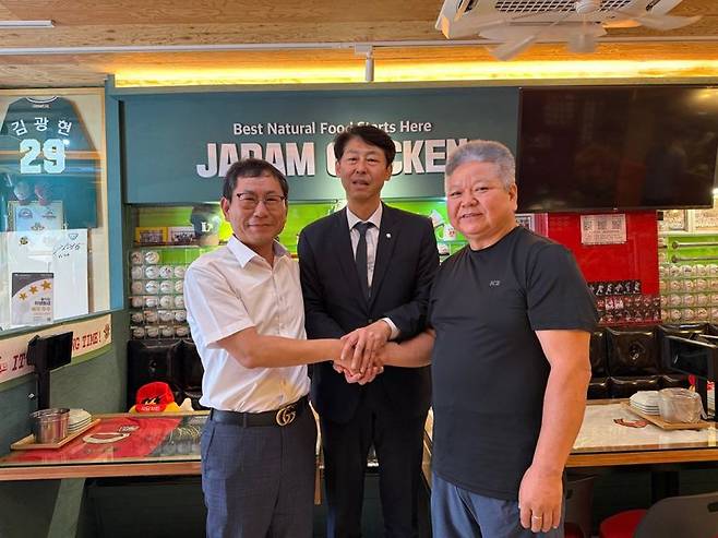 매장 앞 전광판에 정치적 메시지를 담았다는 이유로 폐업할 뻔한 치킨가맹점이 기사회생했다. 사진은 25일 해당 매장을 찾은 나명석 자담치킨 회장이 공식 사과 후 더불어민주당 이훈기 의원, 가맹점주인 황선인씨와 손을 맞잡고 있다. /사진=이훈기 의원 X 계정