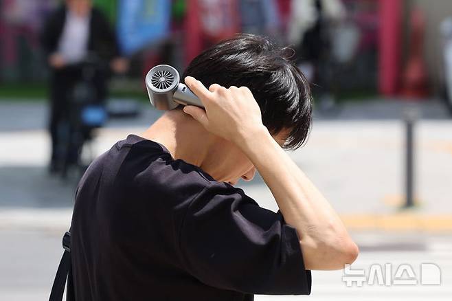 [서울=뉴시스] 권창회 기자 = 전국 대부분 지역에 폭염특보가 발효된 21일 오후 서울 송파구 석촌호수 인근에서 한 시민이 목에 선풍기를 대고 있다. 2025.07.21. kch0523@newsis.com