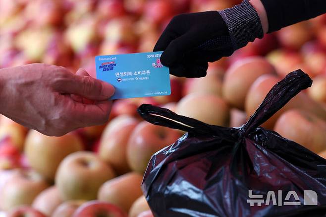 [서울=뉴시스] 조성우 기자 = 소비자심리지수가 4년 만에 최고치를 기록한 23일 서울 시내의 한 전통시장에서 한 시민이 민생회복 소비쿠폰을 이용해 과일을 구매하고 있다. 2025.07.23. xconfind@newsis.com