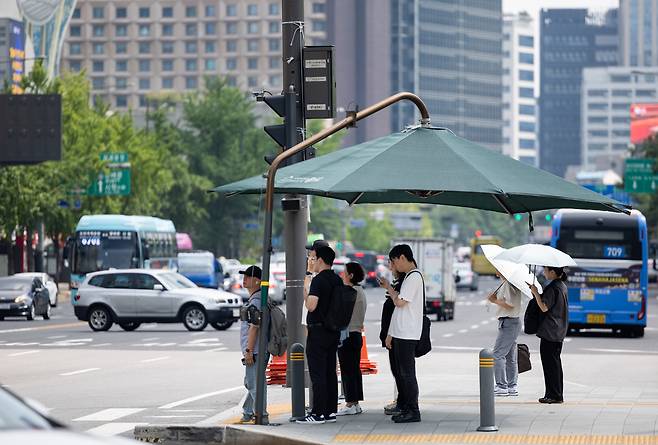 People take shelter from the heat under parasols at Gwanghwamun Square in central Seoul on July 25 as a heat wave warning remains in effect for most parts of Korea. [JOONGANG ILBO]