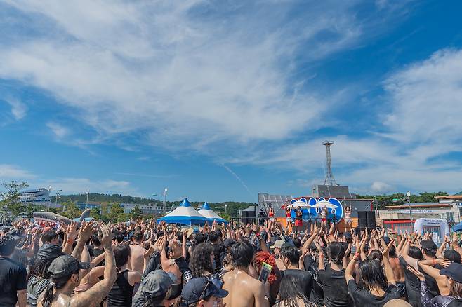 진흙을 바르고 물대포가 쏟아지는 가운데, 특설무대에서 펼쳐지는 공연을 함께 즐기는 관광객들.