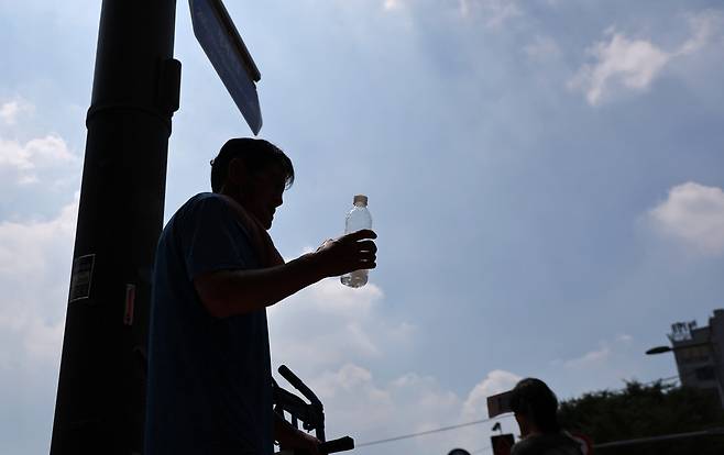 A worker drinks water while moving materials outdoors near the Dongdaemun Shopping Complex in Jung District, central Seoul, on July 27. [YONHAP]