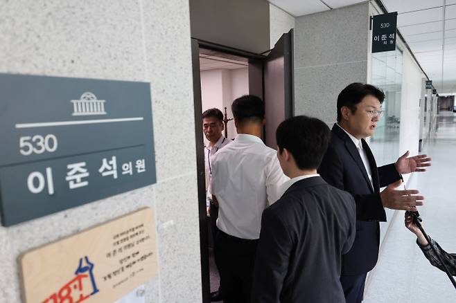 개혁신당 김정철 최고위원이 30일 서울 여의도 국회 의원회관 이준석 의원실 앞에서 ‘김건희특검 관련 압수수색 절차적 문제점 및 준항고 주요 이유 언론 브리핑’을 하고 있는 가운데 특검 관계자들이 압수수색을 위해 의원실로 들어가고 있다.(사진=연합뉴스)