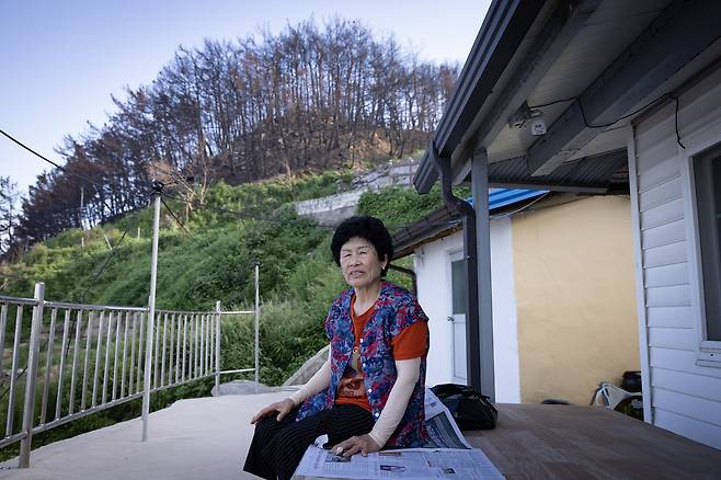 전정영 할머니가 본인의 집 마당 평상에 앉아 주변을 둘러보고 있다. 전 할머니 뒤로 불에 탄 산이 보인다. 불에 탄 나무의 뿌리가 약해져 산사태 위험이 있어 전 할머니도 이재민으로 살아가고 있다. 전민규 기자