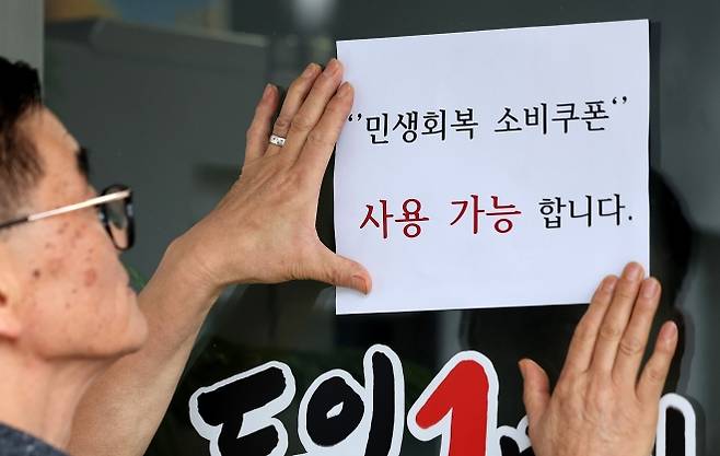 지난 22일 대구 중구 한 음식점 주인이 출입문에 민생회복 소비쿠폰 사용 가능 안내문을 붙이고 있다. 뉴시스