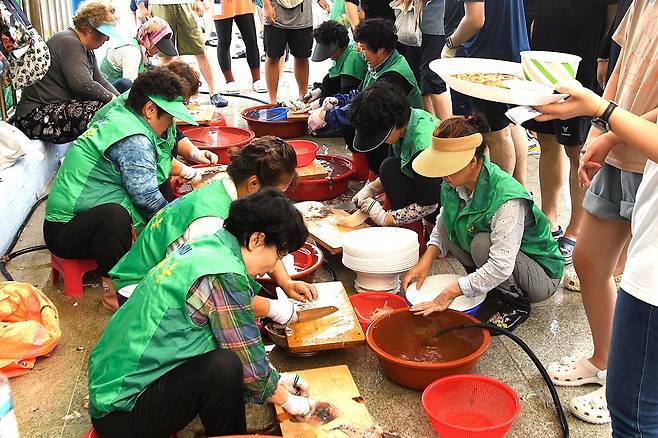 현지 주민들이  참가자들이 맨손으로잡은 오징어를 즉석에서 회로 썰어주는 봉사활동이 펼쳐지고 있다[울릉군 제공]
