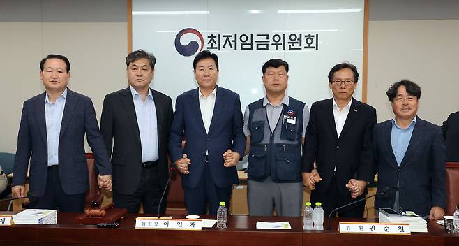 지난달 10일 정부세종청사에서 열린 최저임금위원회 제12차 전원회의에서 내년 최저임금을 시급 1만320원으로 17년 만에 합의로 결정한 공익위원-사용자위원-근로자위원들이 손을 잡고 기념촬영을 하고 있다. 왼쪽부터 하헌제 상임위원, 이인재 위원장, 사용자위원인 류기정 한국경영자총협회 전무, 근로자위원인 류기섭 한국노총 사무총장, 사용자위원인 이명로 중소기업중앙회 인력정책본부장, 공익위원인 권순원 숙명여대 교수. 연합뉴스