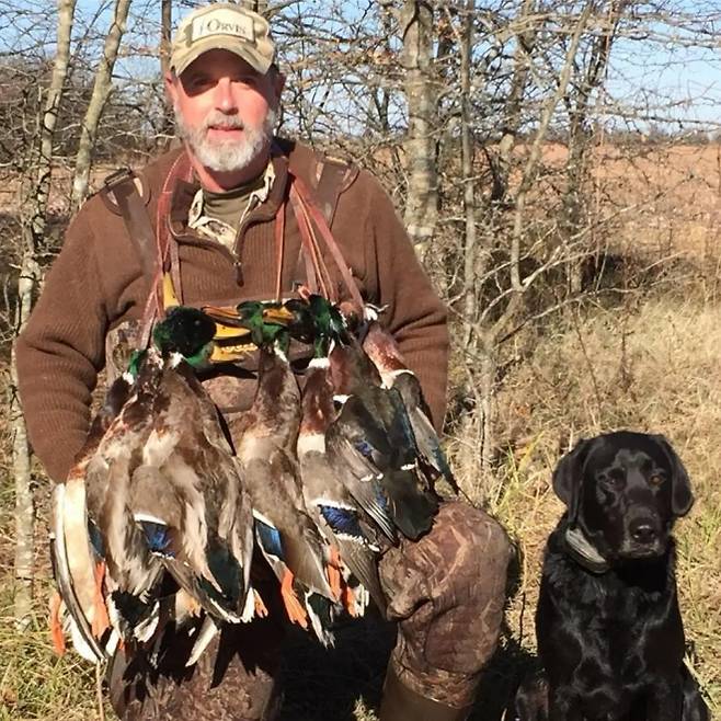 사냥한 물새들을 앞에 두고 포즈를 취한 애셔 왓킨스. 가슴에 사냥한 청둥오리 등 여러 마리의 야생조류를 걸고 앉아 있는 모습이다. 오른쪽에는 함께 사냥에 나섰던 검은색 래브라도 리트리버가 자리하고 있다. 왓킨스는 평소 수렵견과 함께하는 조류 사냥에도 열정을 보였다. 출처=애셔 왓킨스 아웃도어스 페이스북