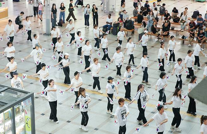 ▲ 제80주년 광복절을 나흘 앞둔 11일 오후 수원시 팔달구 수원역 대합실에서 열린 '광복, 그날의 기쁨 재현하다' 행사에서 권선구 주민자치 댄스 프로그램 수강생들이 태극기를 들고 플래시몹 공연을 하고 있다./전광현 기자 maggie@incheonilbo.com