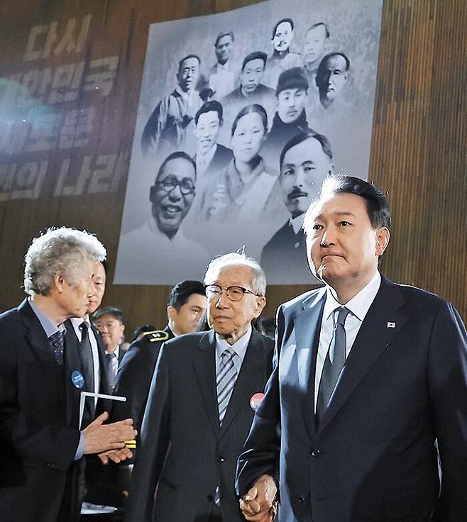 2023년 3월 1일 서울 유관순기념관에서 열린 제104주년 3·1절 기념식에 윤석열 대통령이 김영관 애국지사와 손을 잡고 입장하고 있다. 윤 대통령 뒤에 걸려 있는 현수막에는 김구·안중근·유관순 등 독립운동가의 얼굴 사진이 들어가 있다. 그러나 임시정부 초대 대통령을 지낸 이승만 전 대통령 사진은 없어 논란이 일었다. /연합뉴스