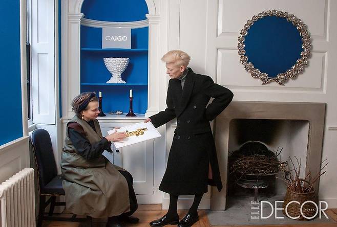 메리애나 케네디와 틸다 스윈턴. 배경은 메리애나 케네디의 집으로, 스트로베리 힐 호텔의 블루 베드룸에서 영감을 받아 푸른색 안료로 칠했다. 주변에 놓인 금박 거울, 러스틱 화병, 레진 촛대, 페인팅 엠블럼(Painting Emblem)은 모두 메리애나의 작품.