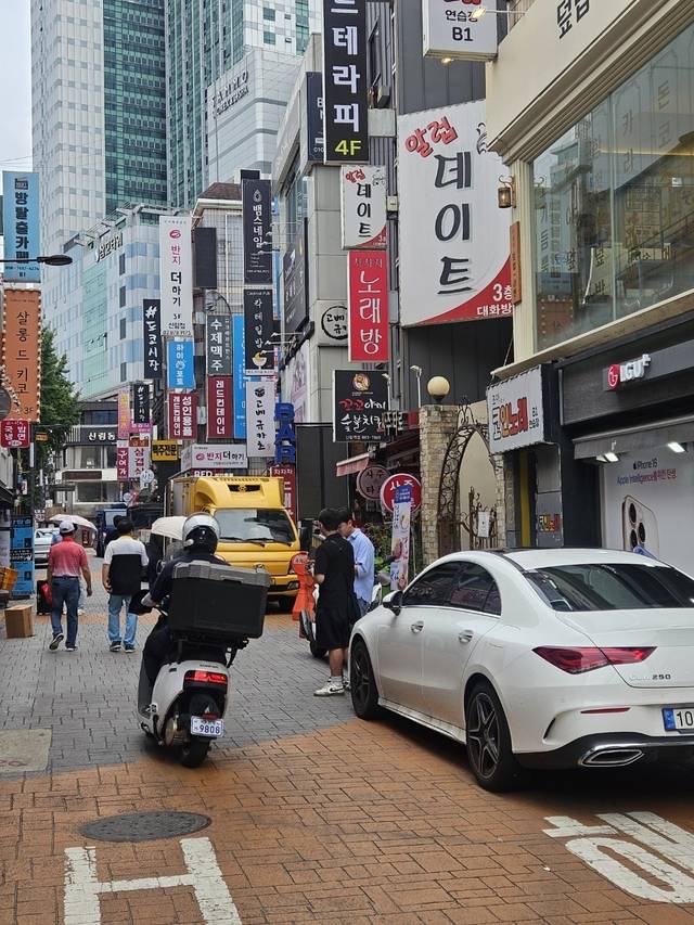 사람 반, 車 반  : ‘차 없는 거리’로 지정돼 있는 서울 관악구 신림역 3∼4번 출구 일대 ‘신림순대타운’ 골목에 11일 낮 트럭과 승용차가 주차된 가운데 오토바이가 달리고 있다.