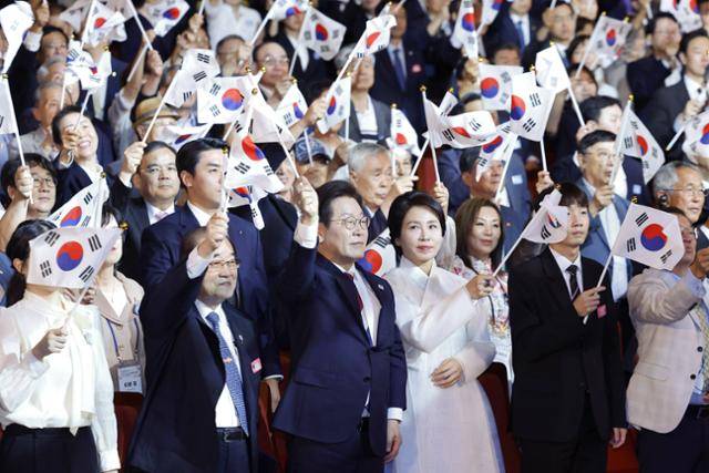 이재명 대통령과 김혜경 여사가 15일 서울 세종문화회관에서 열린 제80주년 광복절 경축식에서 참석자들과 태극기를 흔들고 있다. 뉴시스