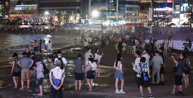 Visitors cool off while watching a drone show at Gwangalli Beach in Busan, Sunday. (Yonhap)