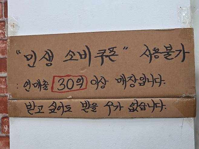 서울 마포구 한 전통시장의 한 야채·과일 가게에 붙은 안내문. 지역별 커뮤니티마다 ‘연 매출 30억원 넘는 동네 점포’가 공유되며 설왕설래가 오간다. /정시행 기자
