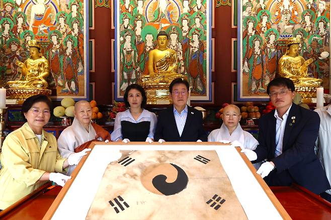 이재명 대통령과 김혜경 여사가 17일 서울 은평구 진관사를 방문해 진관사 주지 법해스님, 더불어민주당 박주민 의원, 김미경 은평구청장과 함께 보물 '진관사 태극기' 앞에서 기념촬영을 하고 있다. 대통령실 제공
