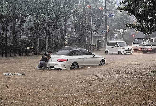 지난 13일 경기 고양시 덕양구 행신로가 폭우로 침수돼 한 시민이 바퀴가 물에 잠긴 차량을 밀고 있다. 이날 덕양구에는 1시간 동안 100㎜ 넘는 폭우가 쏟아졌다./연합뉴스