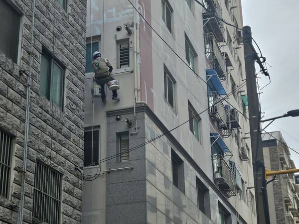 인천의 한 건물에서 노동자가 줄에 몸을 맡긴 채 외벽 도색 작업을 하고 있다.