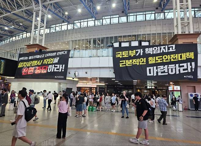 23일 서울역 내 역사에 걸린 '열차운행시 작업 전면 중단'과 '근본적인 철도안전대책 마련'을 촉구하는 현수막 아래에 승객들이 이동하고 있다. 철도노조 제공