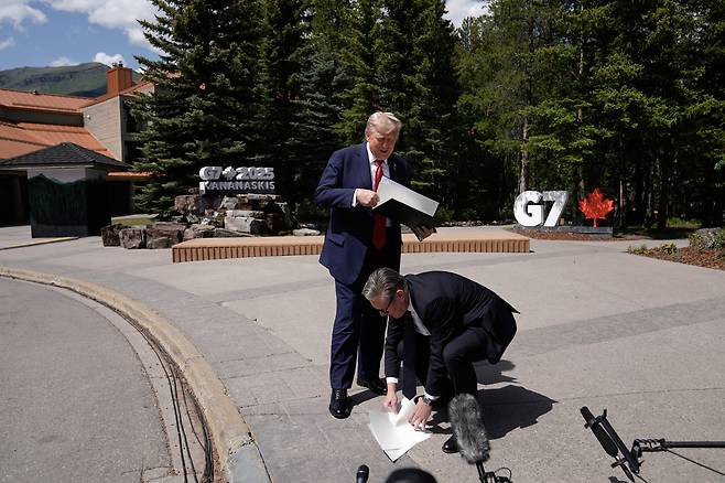 지난 6월 16일 앨버타주 카나나스키스에서 열린 G7 정상회담에서 키어 스타머 영국 총리가 도널드 트럼프 미국 대통령이 떨어뜨린 영-미 무역협정 서류를 줍고 있다./AP 연합뉴스