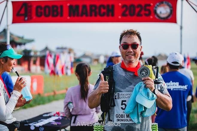 이종민 구진피티에프이 대표가 올 6월 열린 몽골 고비사막 마라톤을 완주한 뒤 완주 메달을 들고 엄지척을 하고 있다. 2023년 칠레 아타카마사막 마라톤을 달린 뒤 “절대 사막에 다신 오지 않겠다”고 다짐했던 그는 “엄청나게 힘들지만, 그 고통을 참으면 말할 수 없는 쾌감과 성취감이 몰려온다”며 다시 사막을 달렸다. 이종민 대표 제공.