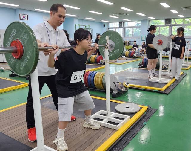 ‘2025 스포츠 영재 캠프’ 참가 여자 초등학생이 역도 종목을 체험하며 전문 지도자의 설명을 듣고 있다. 경기체중·고 제공