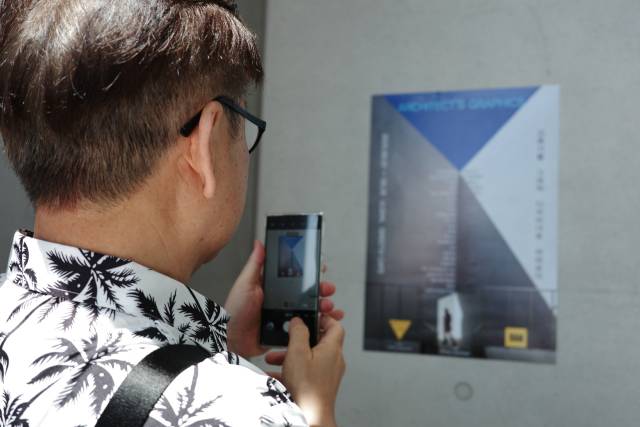 울산 울주군 ‘그릿비 서생점'에서 열고 있는 ‘건축가의 그래픽’ 전시에 참여하는 한 건축가가 전시 포스터를 촬영하고 있다. BAM 제공