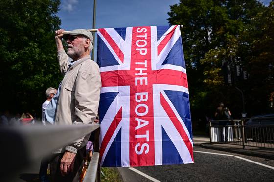 지난달 23일(현지시간) 영국 런던 남쪽 호를리에 있는 난민 수용 시설로 추정되는 쉐라톤 포 포인츠 호텔 밖에서 열린 반이민 시위에서 한 시민이 '배를 멈춰라(Stop The Boats)'라고 쓰인 영국 국기를 들고 있다. AFP=연합뉴스