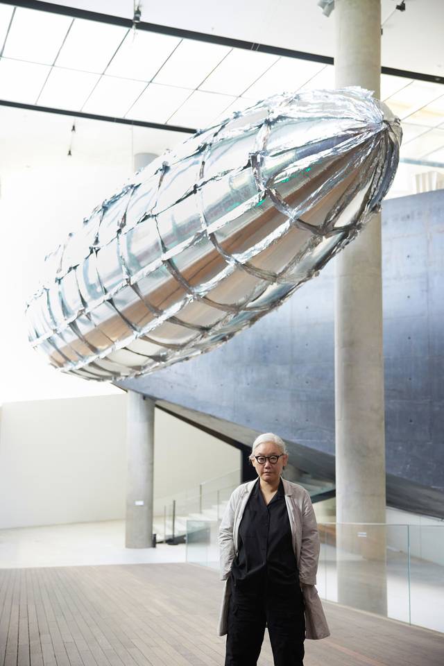 이불 작가가 전시장 입구 천장에 매달린 17m 길이의 은빛 비행선 ‘취약할 의향-메탈라이즈드 벌룬’ 아래서 포즈를 취하고 있다. ⓒLee Bul, 리움미술관 제공