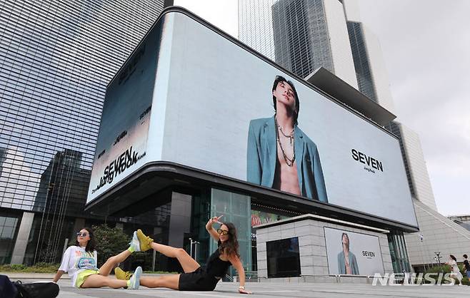[서울=뉴시스] 황준선 기자 = 2023년 25일 오후 서울 강남구 코엑스 케이팝 스퀘어 전광판 앞에서 외국인 관광객들이 방탄소년단(BTS) 멤버 정국의 솔로 싱글 '세븐(SEVEN)'의 광고물을 배경으로 기념촬영을 하고 있다. 2023.07.25. hwang@newsis.com