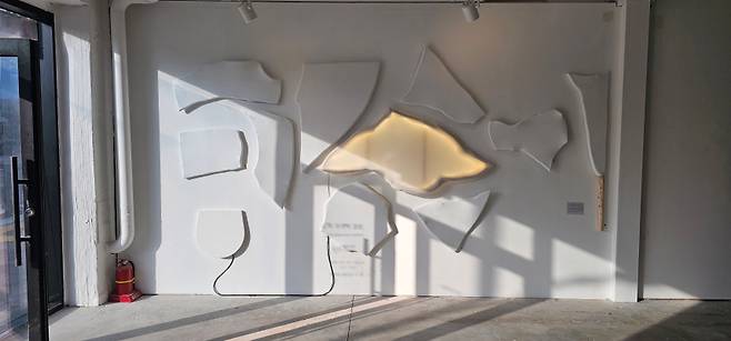 김상균 작가의 설치. 흩어진 조각들이 벽면에 놓이면서 내부의 빛은 발광하듯 새어 나온다. 파편은 단절이 아니라 또 다른 연결을 모색하는 유기체로 기능한다.