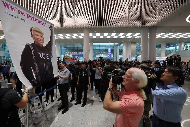 미국 이민당국에 의해 조지아주에 구금됐던 한국인 근로자들이 귀국한 12일 인천국제공항 제2여객터미널 입국장에서 도널드 트럼프 미국 대통령 얼굴 배너를 든 시민단체가 시위하고 있다. 공항사진기자단