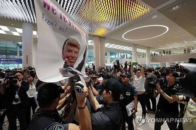 시위 저지하는 공항경찰대 (영종도=연합뉴스) 이진욱 기자 = 미국 이민당국에 의해 조지아주에 구금됐던 한국인 근로자들이 귀국한 12일 인천국제공항 제2여객터미널 입국장에서 공항경찰대가 도널드 트럼프 미국대통령 얼굴 배너를 든 시민단체의 시위를 저지하고 있다. 2025.9.12 cityboy@yna.co.kr