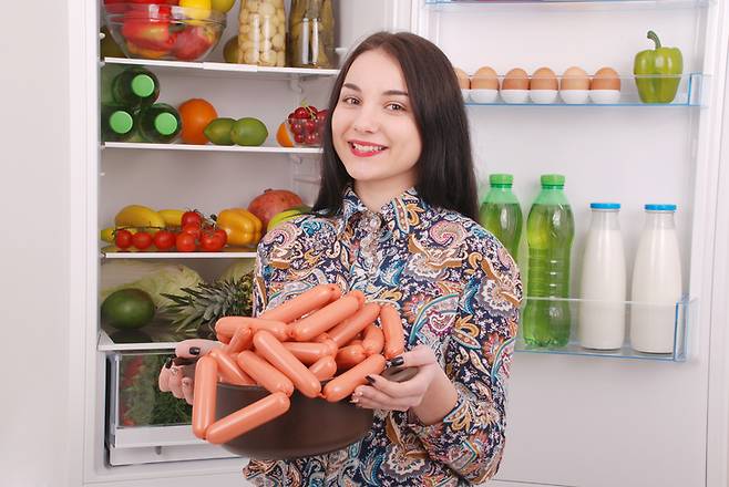 소시지 베이컨 삼겹살 등 포화지방이 많은 고지방 음식을 4일만 먹어도, 뇌의 해마에 당장 이상한 변화가 생기는 것으로 생쥐실험 결과 나타났다. 여성이 냉장고 앞에서 주렁주렁 달린 소시지를 내보이고 있다.[사진=게티이미지뱅크]