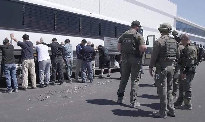 지난 4일(현지시간) 미국 조지아주 서배너에 위치한 현대차그룹·LG에너지솔루션의 합작 배터리 공장(HL-GA 배터리회사) 건설 현장에 미국 이민세관단속국(ICE) 요원들이 들이닥쳐 실시한 단속 영상을 ICE가 6일 공개했다. 체포된 공장 직원들이 다리에 수갑을 채우기 위해 차량 벽에 손을 대고 대기하고 있는 모습을 ICE 요원들이 지켜보고 있다. ICE 제공