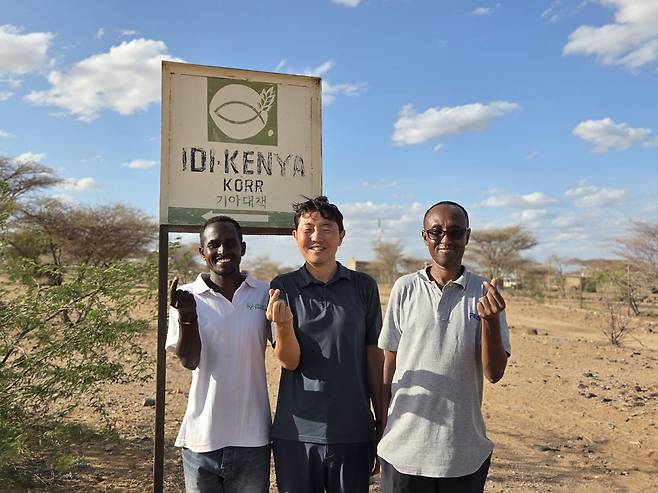 후세인과 그랜트가 케냐 마르사빗주에 위치한 기아대책 코어지부 표지판 앞에 현지 선교사와 함께 서 있는 모습.