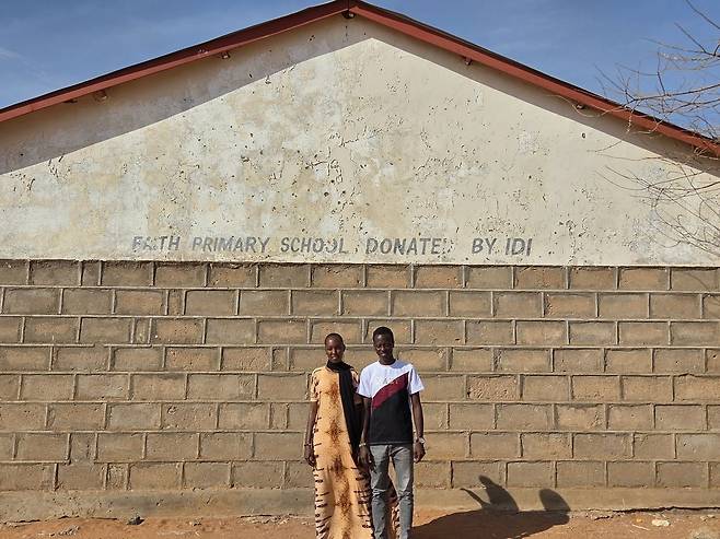 말말로 차우레와 나씨보 미르기찬이 교사로 봉사하고 있는 케냐 코어의 믿음초등학교 앞에 서 있다.