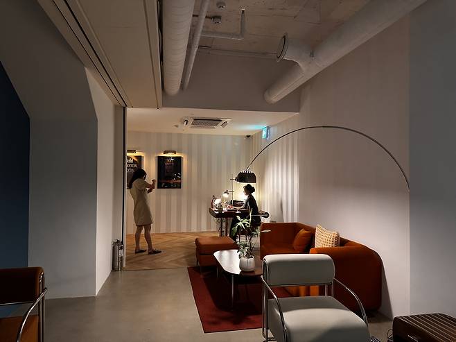 The basement lounge blends deep orange armchairs, striped walls and low lighting to create a quiet, semi-private space beside the AI demo area. (Moon Joon-hyun/The Korea Herald)