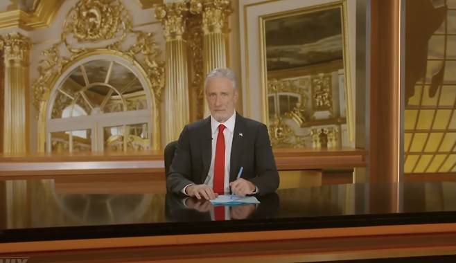 ABC의 '데일리 쇼' 호스트 존 스튜어트가 도널드 트럼프 대통령의 마러라고 별장을 연상시키는 금색 세트에서 트럼프 대통령이 즐겨 입는 빨간색 넥타이를 매고 정장을 입으면서 행정명령에 서명하는 흉내를 내고 있다. (사진=데일리쇼 유튜브 갈무리)