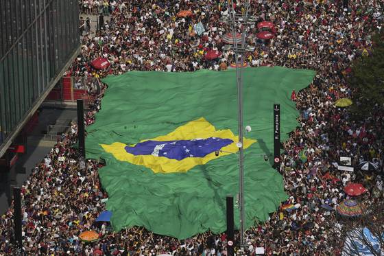 21일(현지시간) 브라질의 리우데자네이루에서 열린 자이르 보우소나르 전 대통령 사면 반대 시위에서 참석자들이 대형 브라질 국기를 내걸고 행진하고 있다. [AP=연합뉴스]