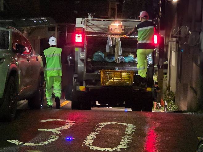 불안한 일터 쓰레기 수거 작업 중인 환경미화원이 25일 새벽 서울의 한 대학가 인근 골목에서 수거차 발판에 올라탄 채 이동하고 있다. 우혜림 기자
