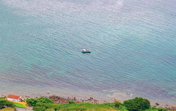 산에서 내려다본 사량도 바다 풍경. 잔잔한 바다 위에 배 한 척이 한가로이 떠 있다.