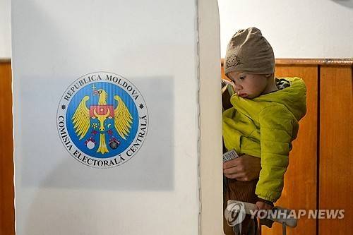 28일 몰도바 총선 (키시나우 AFP=연합뉴스) 28일 총선 치러지는 몰도바에서 한 유권자가 아이를 안고 투표하고 있다. 2025. 9. 28.